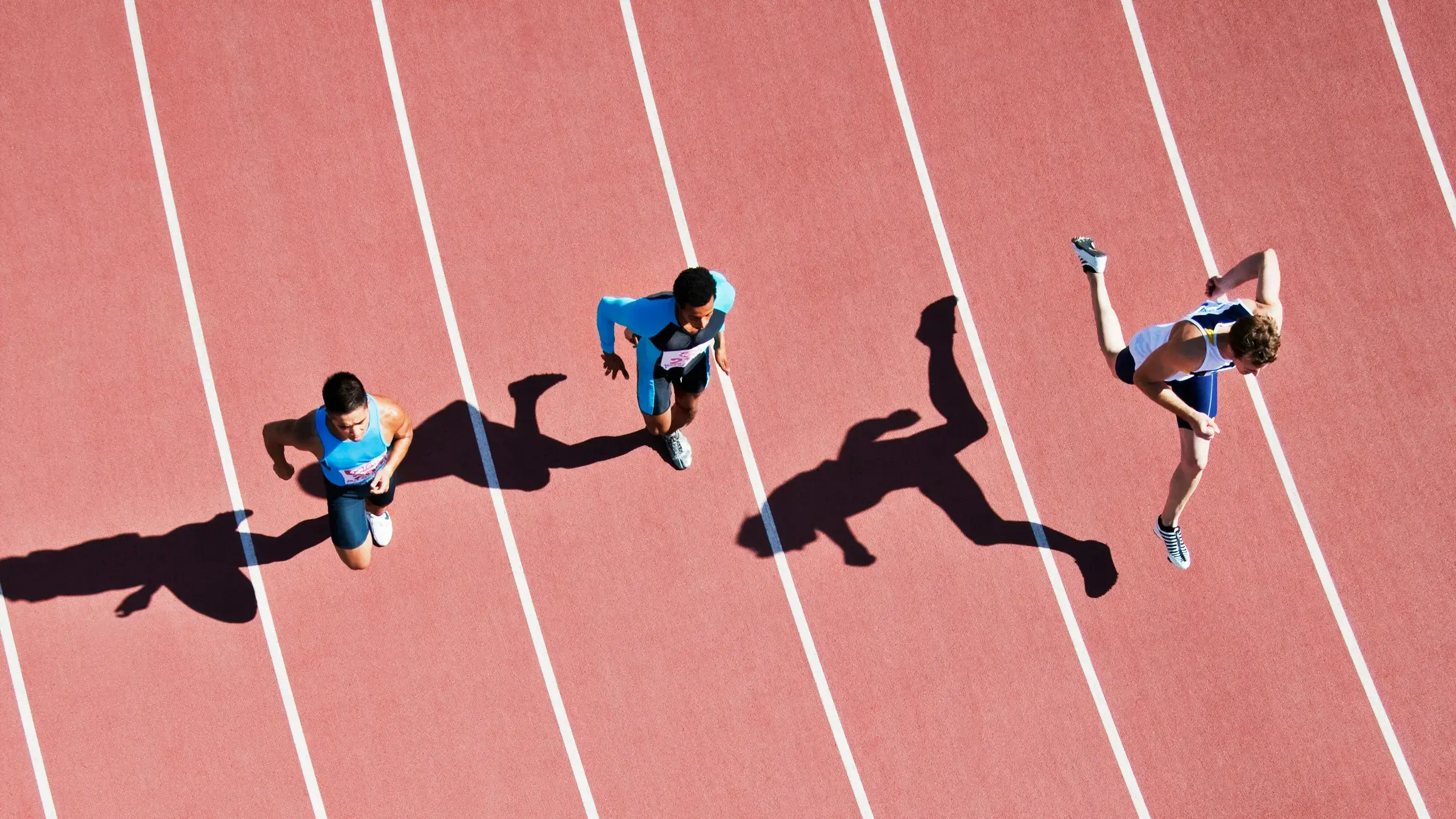 Three runners sprinting in separate lanes, seen from above