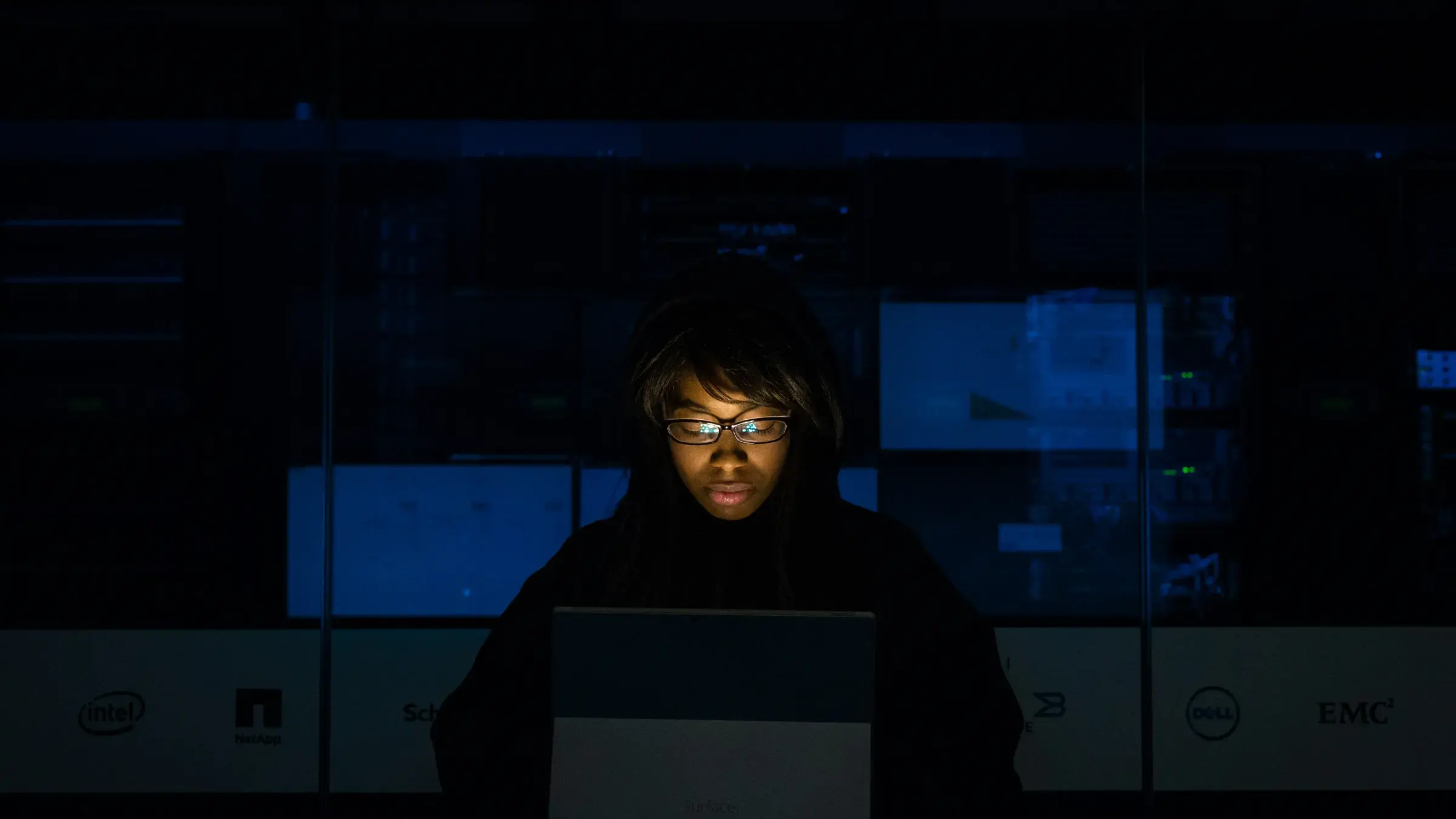 Person working on a laptop in front of a dark server room